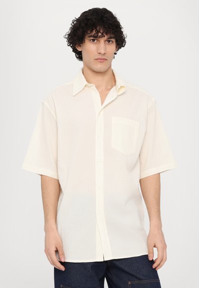 Chemise à manches courtes boutonnées en tissu texturé blanc cassé avec une poche poitrine et un col classique, dotée d'une coupe décontractée et d'un ourlet droit.