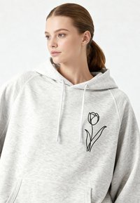 Felpa con cappuccio grigio chiaro in tessuto morbido, con tasca frontale e grafica di un tulipano nero sul lato sinistro del petto. Coulisse sul cappuccio.