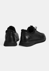 Baskets noires en cuir lisse avec une forme arrondie, semelle en caoutchouc texturé et design minimaliste. Elles disposent de lacets et d'une languette à l'arrière.