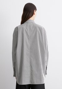 Chemise à manches longues rayée en noir et blanc, dotée d'un col ajusté, d'épaules tombantes et de poignets à boutons. Tissu doux avec des lignes verticales.