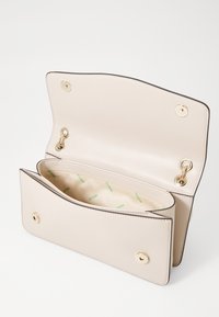 Borsa in pelle beige con accessori in oro, dotata di chiusura a linguetta, tasche interne e fodera con stampa del logo. Design strutturato con texture liscia.