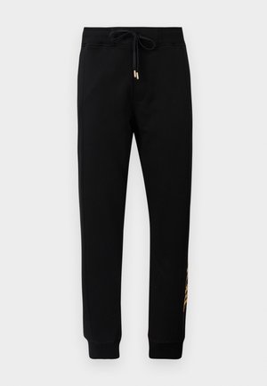 Sorte tapered joggebukser med snor i livet og ribbede mansjetter, med gullbokstaver på venstre ben.