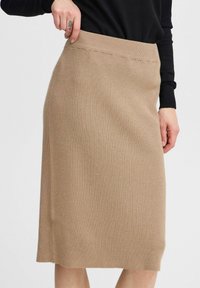 Jupe crayon en tricot beige clair avec une texture côtelée, dotée d'une taille haute et d'une coupe droite, atteignant juste en dessous du genou.