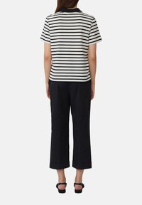 Gestreepte zwart-witte polo met korte mouwen, gecombineerd met donkere, cropped broeken met omgeslagen manchetten en zwarte sandalen.