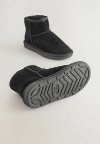 Schwarze Wildleder-Ankle-Boots mit einem weichen Futter, ausgestattet mit einer flexiblen grauen Gummisohle mit einem Chevron-Muster und verstärkten Nähten.