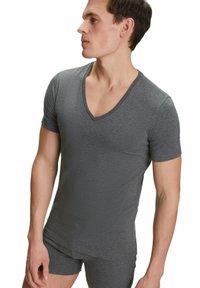 Maglietta grigia a maniche corte con scollo a V, realizzata in tessuto morbido ed elastico, caratterizzata da un design aderente e una texture liscia, indossata con pantaloni shorts coordinati.