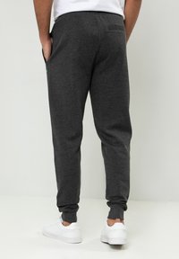 Dunkelgraue Jogginghosen aus weichem Stoff, mit elastischen Bündchen, seitlichen Taschen und einem kleinen grünen Logo auf der linken Tasche.