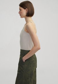 Top sin mangas beige con tirantes finos, combinado con pantalones verde oliva que presentan bordados florales y bolsillos laterales. Textura suave, diseño informal.