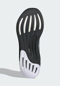 Schwarze Laufsohle aus strukturiertem schwarzem Gummi mit weißen Abschnitten. Verfügt über Rillen und Aussparungen für Grip und Flexibilität.