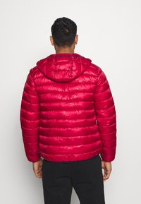 Rød polstret jakke med hætte, der har horisontale syninger og en skinnende overflade, designet til varme og dækning.