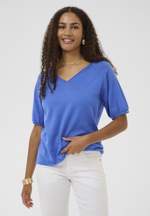 Top albastru cu mâneci scurte și decolteu în V, cu croială lejeră. Țesătură ușoară cu textură subtilă. Asortat cu pantaloni albi și accesorii aurii.