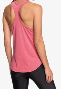 Top atletico rosa con design a corsetto, caratterizzato da una finitura texture e un orlo arrotondato, abbinato a leggings neri.