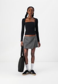 Zwarte lange mouw top met vierkante halslijn, gestreepte plissé minirok, zwarte sneakers en witte enkelkousen. Draagt een zwarte schoudertas.
