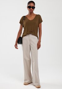 Oliwkowa, krótki rękaw, koszulka polo w dekoltem w serek, w zestawieniu z beżowymi, szerokimi spodniami oraz brązowymi butami typu slip-on. Czarna torba z łańcuszkiem, duże okulary przeciwsłoneczne.