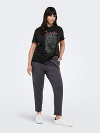 Black graphic T-shirt featuring a leopard print and the word "Wild" in pink. Gray tapered pants; white sneakers with black accents.