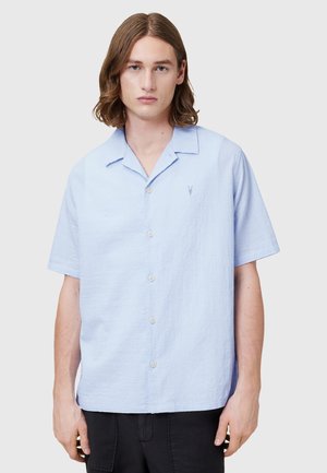 Camicia azzurra a maniche corte con bottoni in tessuto testurizzato, dall'aspetto leggermente stropicciato e un piccolo logo ricamato sul petto.