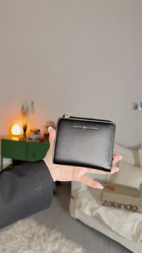 Schwarze Lederbrieftasche mit strukturierter Oberfläche, mit goldenem Logo und Reißverschlussverschluss. Kompaktes rechteckiges Design, leicht zu halten.