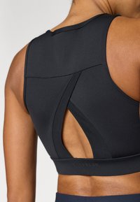 Μαύρο αθλητικό σουτιέν με σχέδιο racerback και λεπτομέρεια κοψίματος, κατασκευασμένο από απαλό, ελαστικό υλικό, που αναδεικνύει μια εφαρμοστή σιλουέτα.