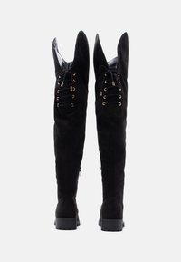 Mustat korkokengät, joissa on terävät kärjet, valmistettu mokasta. Varustettu nauhoilla ja kultasävyisillä rei'illä. Pohja on teksturoitu pidon parantamiseksi.