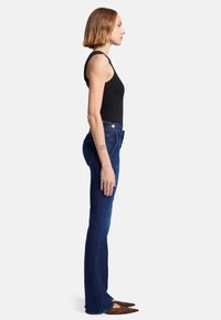 Jeans in denim a palazzo di colore scuro con una trama liscia e una leggera elasticità. Abbinati a un top senza maniche nero e scarpe a punta con stampa leopardata.