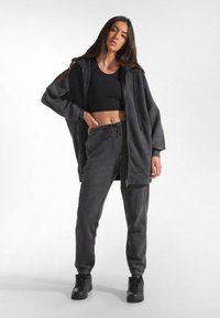 Felpa nera oversize con zip e coulisse, abbinata a pantaloni jogger coordinati. Tessuto morbido, vestibilità comoda e polsini a costine. Sneakers nere.