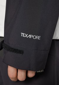 Mâneca unei jachete negre TEXAPORE, prezentând o curea cu arici, cusături vizibile, o textură elegantă și un logo alb pe o suprafață mată.