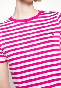 Camiseta a rayas fucsia y blanca con cuello redondo. Presenta un logotipo sutil en negro en el lado izquierdo. Mangas cortas, material de algodón.