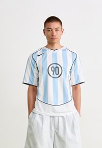 Nike-drakt med lyseblå og hvite vertikale striper, svarte detaljer, og en sirkulær svart grafikk med "90" på forsiden.