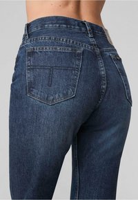 Dunkelblaue Jeans aus Denim mit einer figurschmeichelnden Form, detaillierten Nähten, zwei Gesäßtaschen und einem hohen Bund. Strukturierter Stoff sichtbar.