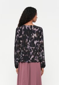 Langarmbluse in Schwarz mit einem lila abstrakten Muster. Leichte Stoffqualität, lockere Passform und elastische Bündchen.