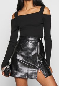 Schwarzes, geripptes Off-Shoulder-Oberteil mit langen Ärmeln, kombiniert mit einem glänzenden, schwarzen Minirock mit Krokodilstruktur und seitlichem Reißverschluss.