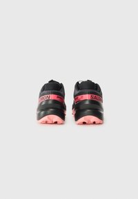 Chaussures de course noires avec des accents roses. Elles possèdent une semelle rembourrée, un dessus en tissu texturé et des poignées à l'arrière pour un enfilage facile.