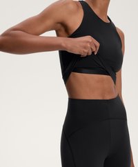 Musta urheiluliivi ja korkeavyötäröiset leggingit, joissa on sileä pinta ja saumatonta muotoilua. Liiviä vedetään poispäin vartalosta.