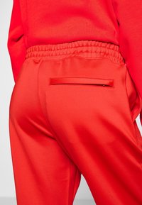 Rode, elastische taillebroek met een gladde textuur; heeft een achterzak met een eenvoudige flap; aansluitend ontwerp.