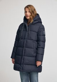 Marinblå pufferjacka med huva, utrustad med en quiltad design, justerbara dragsnören och sidofickor. Tillverkad av ett smidigt, vattentåligt material.