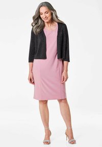 Rosa Etuikleid mit einer schwarzen, glitzernden Strickjacke. Silberne Sandalen. Die Strickjacke hat Dreiviertelärmel; das Kleid weist dezente Perlendetails am Ausschnitt auf.