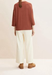Top oversize color ruggine con maniche a tre quarti, abbinato a pantaloni larghi color crema e stivaletti con plateau marroni. Tessuto morbido e vestibilità rilassata.