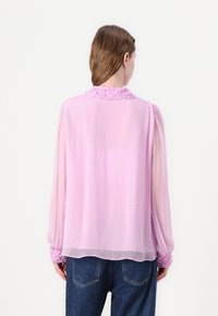Leichte rosa Bluse mit langen Ärmeln, texturierten floralen Details am Kragen und an den Manschetten, kombiniert mit Jeans.