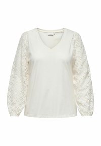 Hvit V-hals topp med strukturerte blondepufmermer, med glatt liv og elastiske mansjetter, som fremhever intrikate geometriske mønstre.