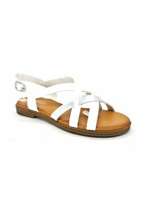 Sandale plate blanche avec des brides croisées, boucle à la cheville, et semelle coussinée beige avec un dessous texturé pour l'adhérence.