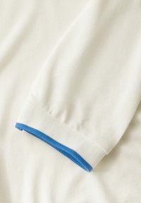 Maglietta bianca a maniche lunghe con tessuto testurizzato e accento in blu a costine sui polsini. Il design presenta una vestibilità classica e casual.