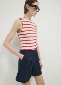 Débardeur en tricot avec des rayures rouges sur fond crème, associé à un short bleu marine avec des plis sur le devant, des poches et une coupe décontractée.