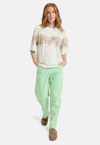 White T-shirt with brown floral design, paired with light green loose-fitting pants and brown slip-on shoes. Casual style, relaxed fit.