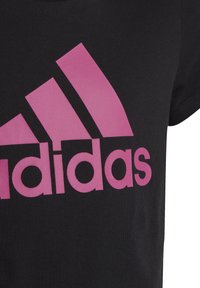 T-shirt in cotone nero con un grande logo Adidas rosa e un design con tre strisce rosa sul lato sinistro, maniche corte e collo rotondo.
