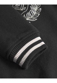 Čierna mikina so štruktúrovanou tkaninou a ribbed manžetou s čierno-bielymi pruhmi. Vyšitý dizajn na tele.