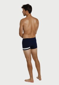 Marineblaue Badeshorts mit weißen horizontalen Streifen an den Seiten, aus glattem Stoff gefertigt, der eng anliegt und gleichzeitig bequem ist.