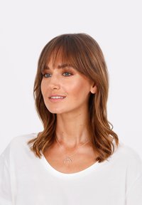 Silberne Halskette mit einem Anhänger in Form eines Halbmonds, getragen über einem weißen T-Shirt. Verfügt über eine glatte Metalloberfläche und ein dünnes Kettendesign.