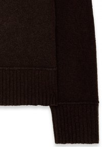 Détail d'un pull brun présentant une texture douce, des poignets et un ourlet côtelés. Le tissu semble épais et chaud avec une couleur unie et sans motifs visibles.
