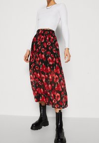 Gonna floreale rossa e nera realizzata in tessuto leggero, con un design fluente e una vita elasticizzata, abbinata a stivaletti neri.