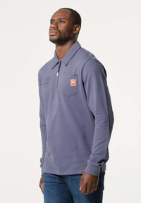 Langsleeve polo in lila katoen, met een kraag, ritssluiting, borstzak aan de linkerzijde en geborduurd logo. Eenvoudig ontwerp met geribde manchetten.